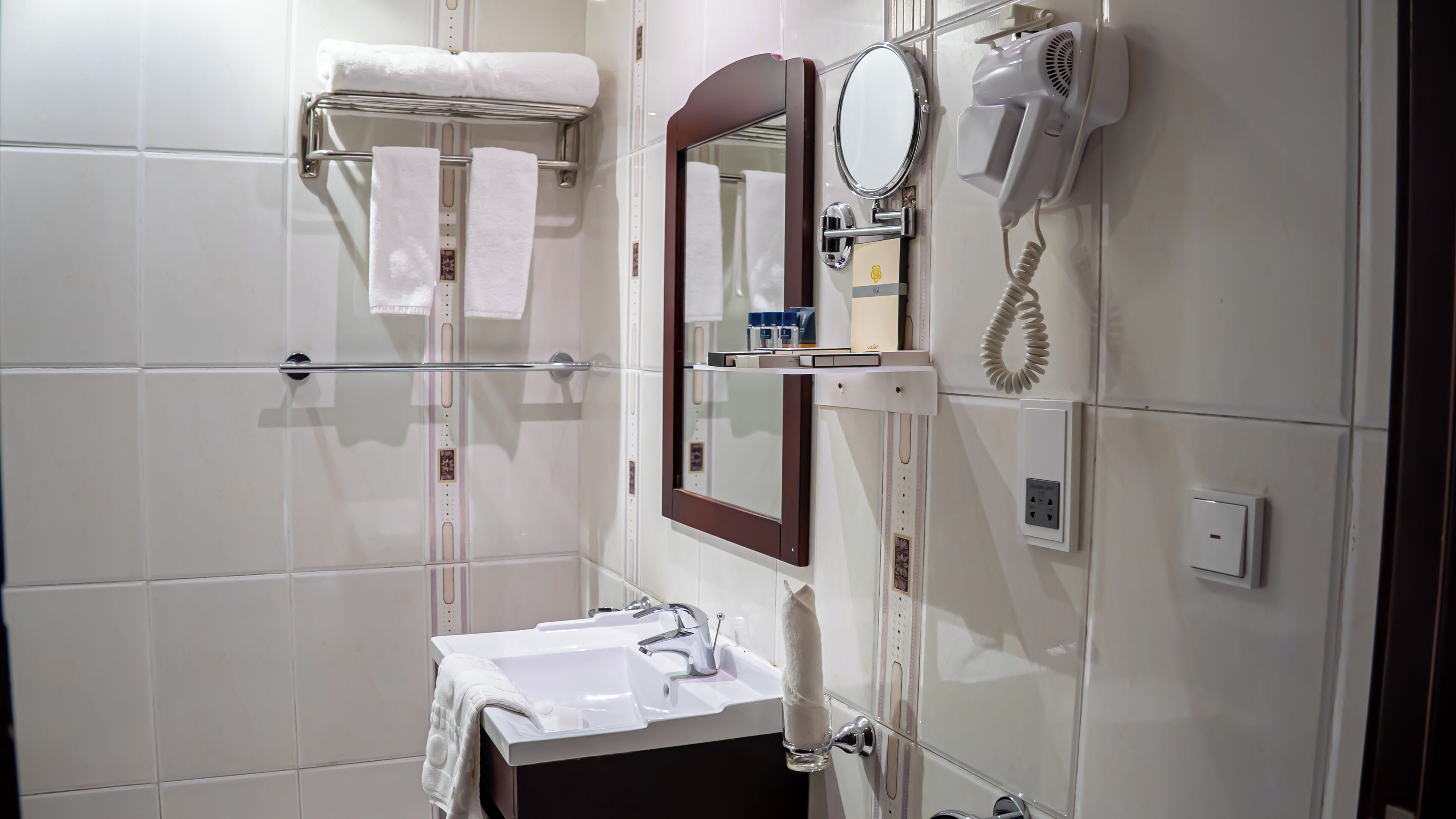 A bathroom with a sink, mirror, towel rack, hairdryer, and a glass of water.