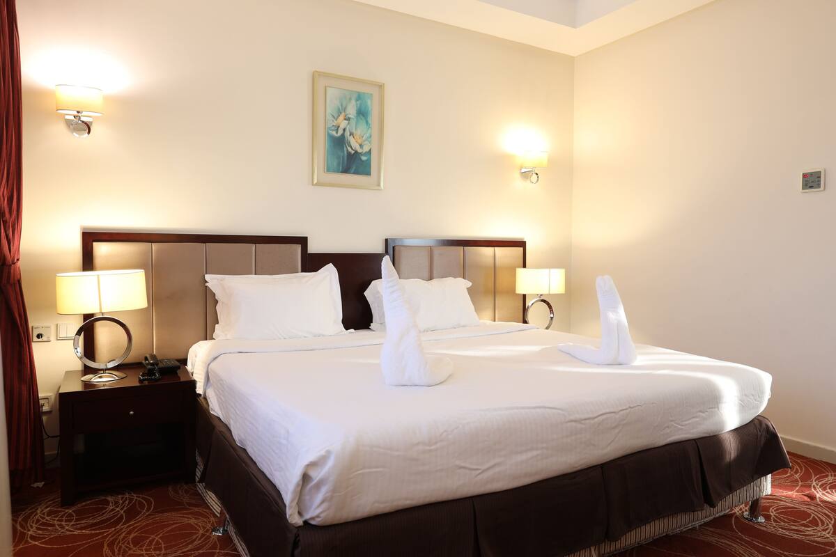 A hotel room with a large bed, two bedside lamps, a nightstand, and a painting on the wall.