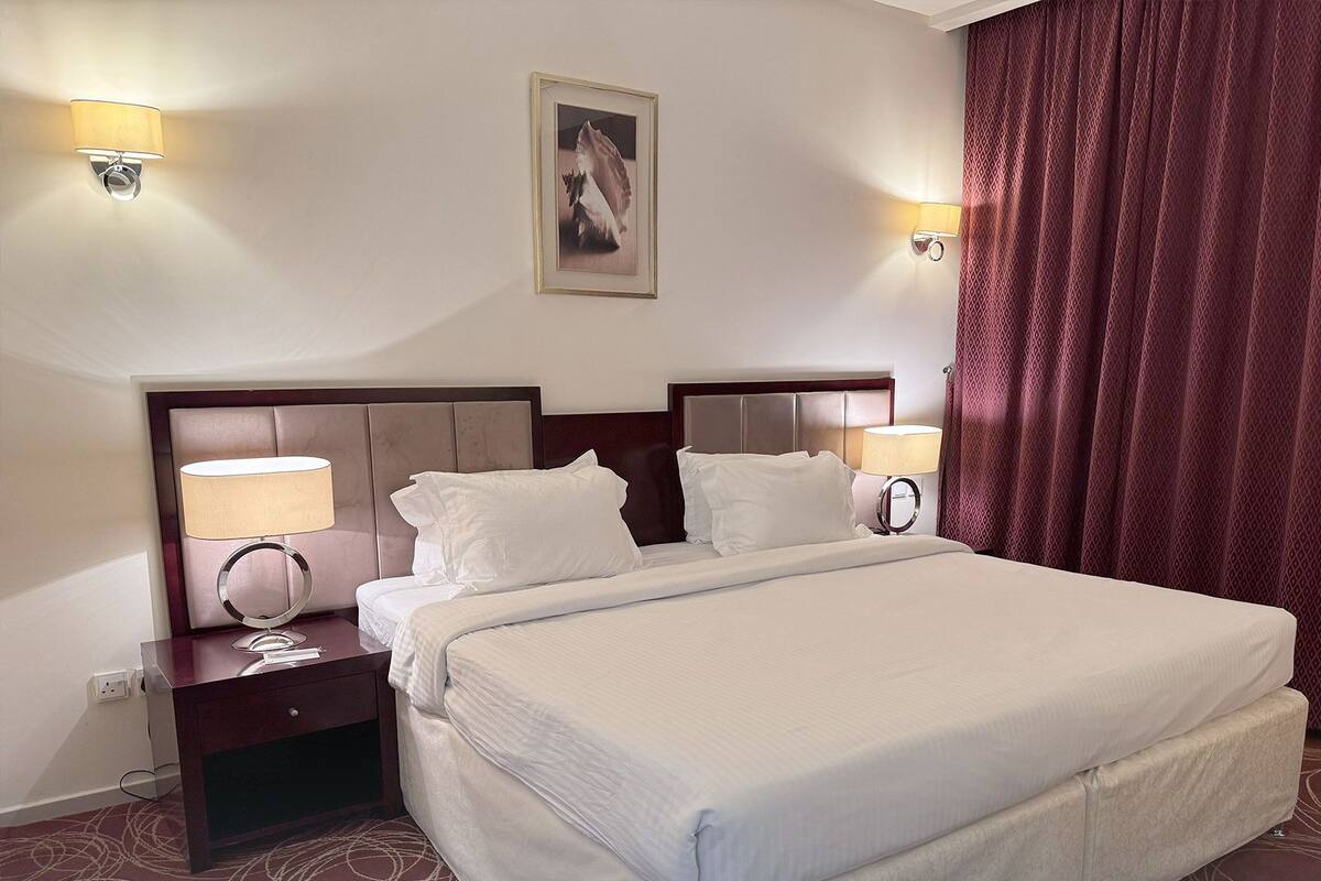 A hotel room with a large bed, two bedside tables with lamps, a framed picture on the wall, and a red curtain.