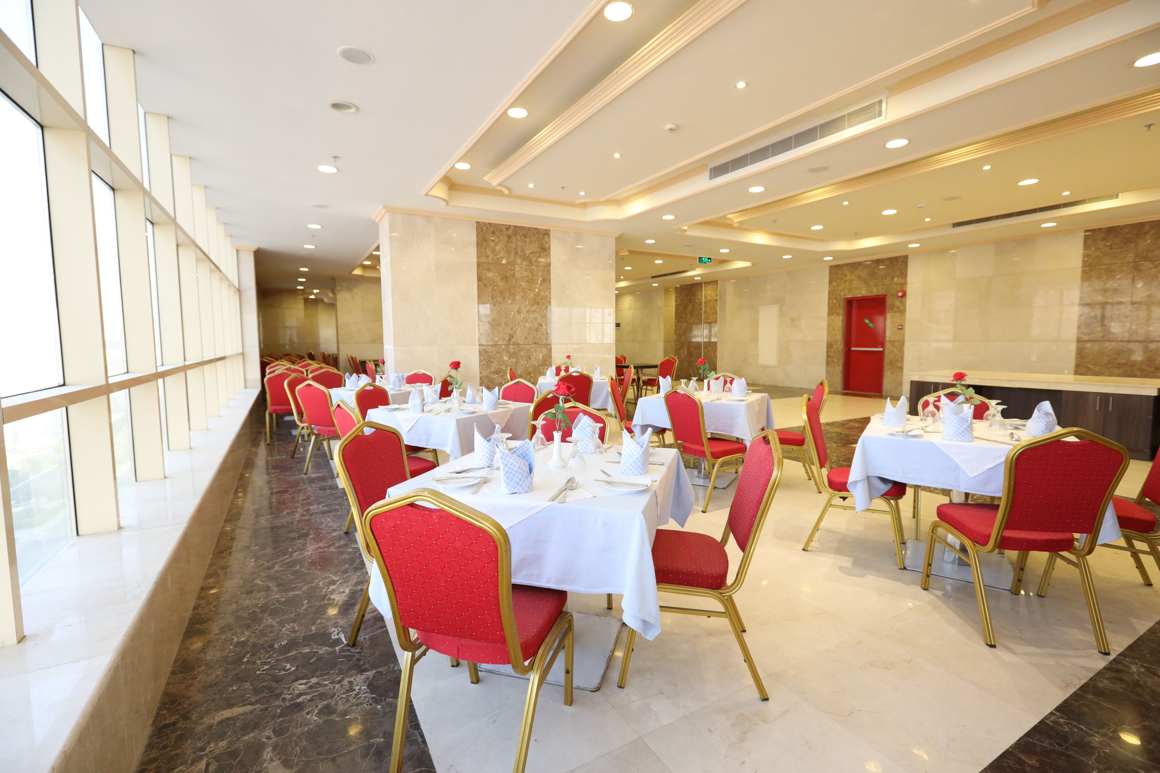 Une salle de banquet avec de nombreuses tables rondes, des chaises rouges et des nappes blanches.