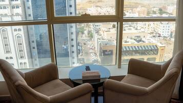 Una habitación con dos sillones color beige, una mesita redonda y vistas a un paisaje urbano a través de amplios ventanales.