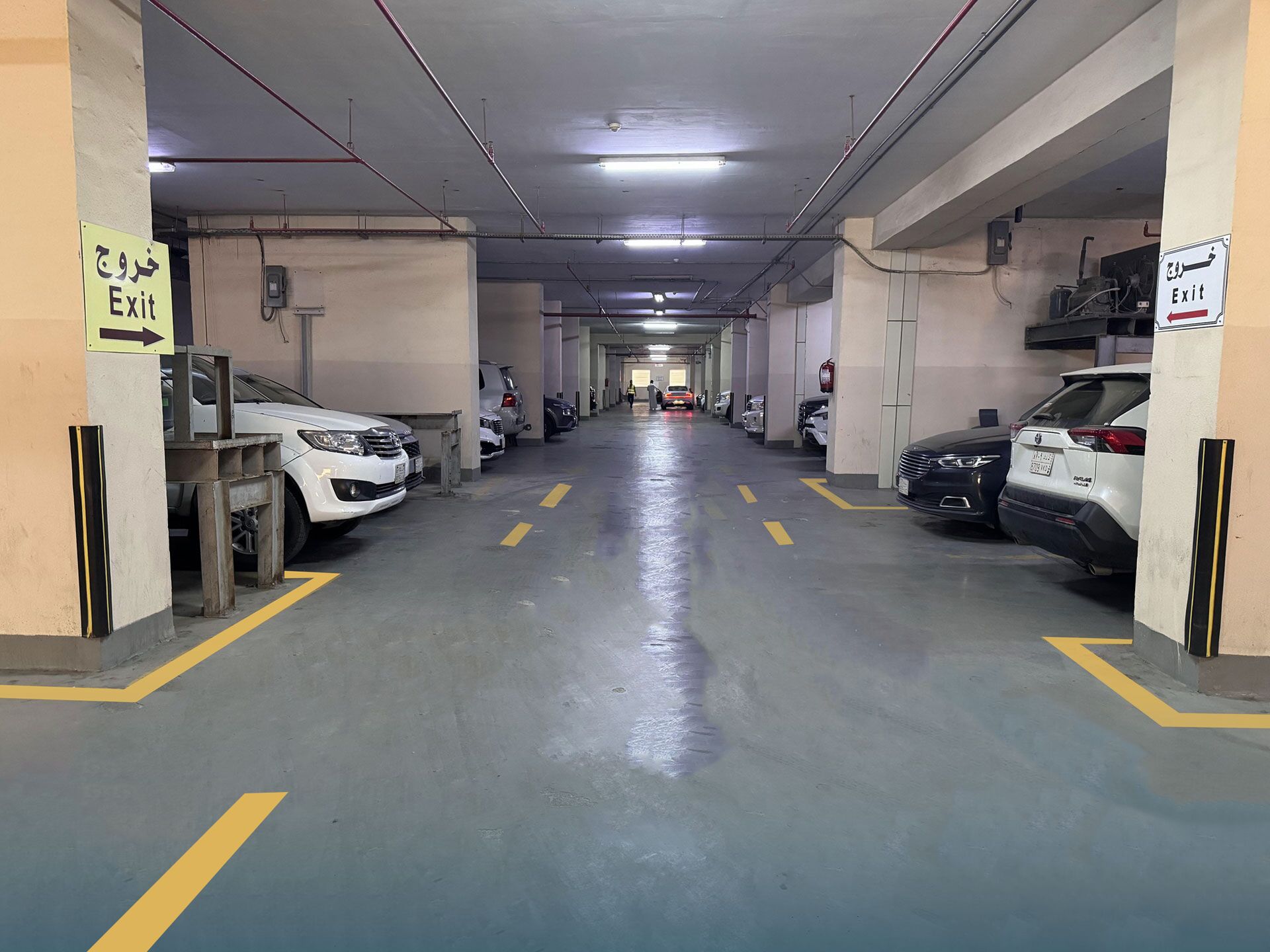Un aparcamiento de varios niveles con coches estacionados a ambos lados y señales de salida en las paredes.