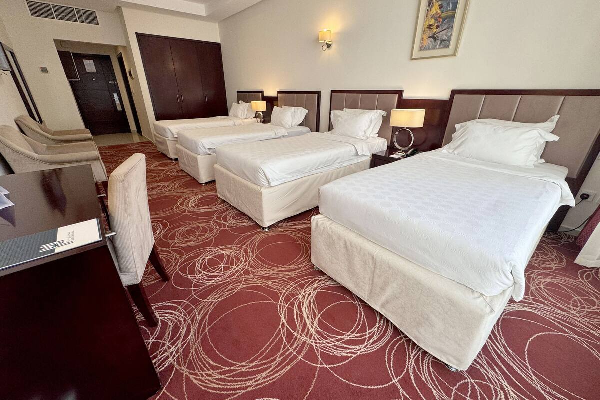 A hotel room with three beds, a desk, and a chair.