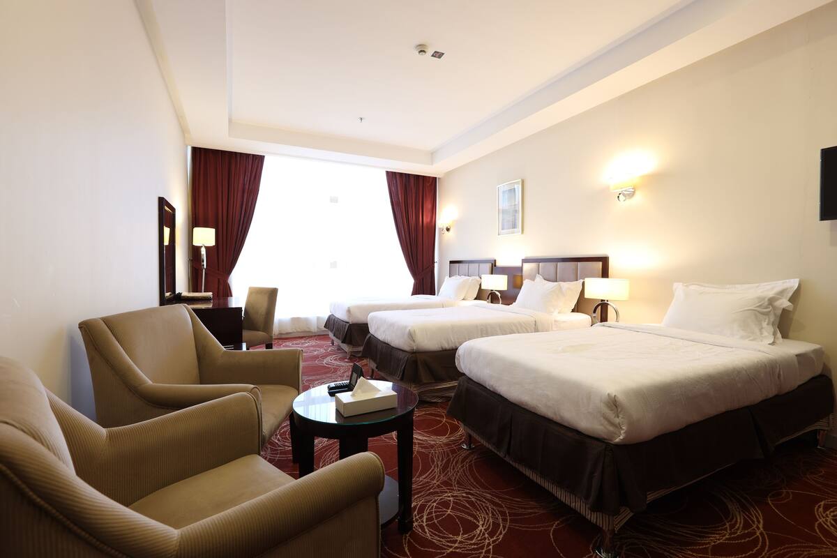 A hotel room with two beds, a sofa, a small table, and a TV.