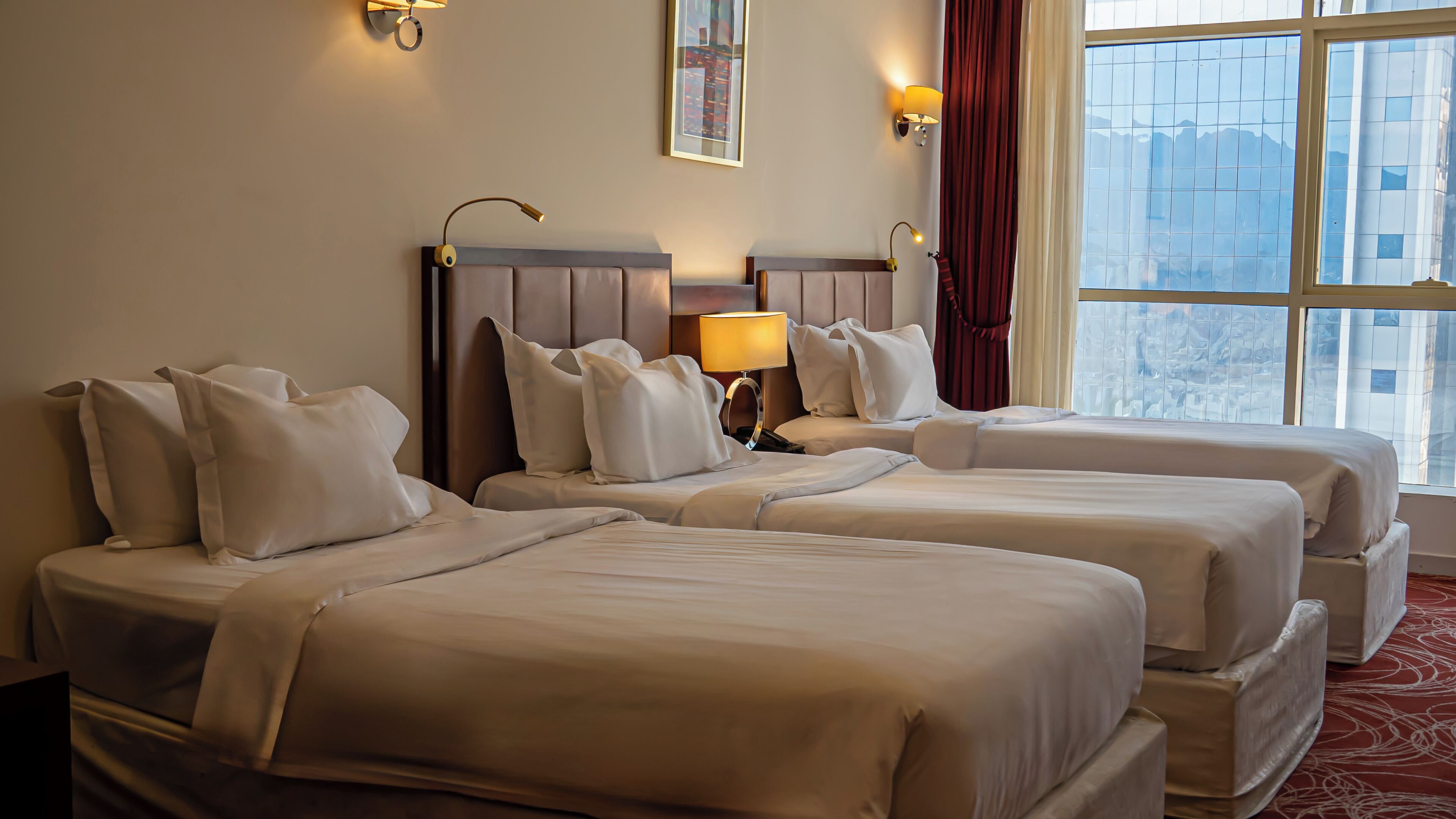 A hotel room with two beds, a large window with a view, and a red curtain.