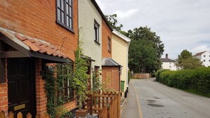 A narrow street lined with traditional brick houses, a wooden fence, and a clear road. - Cosy Cottage with log burner, in the hart of the Norfolk countryside (Buxton)