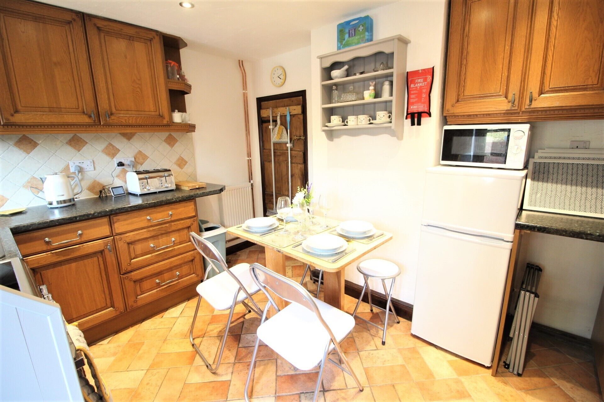 A compact kitchen with wooden cabinets, a microwave, a refrigerator, and a dining table set for four.