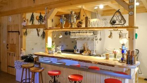 Ett rustikt kök med synliga träbjälkar, en köksö med barstolar, upphängda köksredskap och diverse köksutrustning.