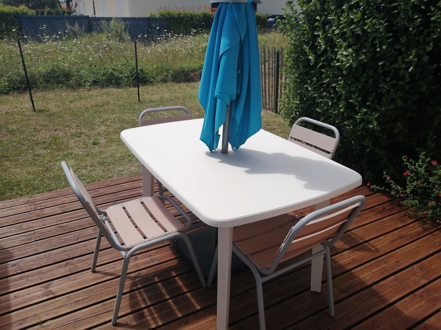 Une terrasse avec une table blanche et deux chaises, un parasol bleu et un plancher en bois.