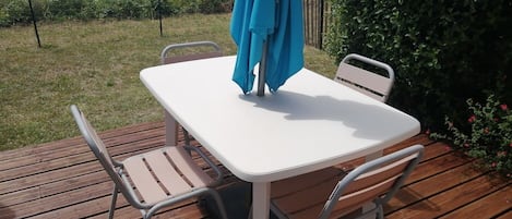 Une terrasse avec une table blanche et deux chaises, un parasol bleu et un plancher en bois.