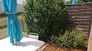 Eine Holzterrasse mit einem weißen Tisch und Stühlen, umgeben von Grünpflanzen und einem Holzzaun.