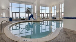 An indoor swimming pool with clear glass walls, a blue chair, and a palm tree outside. - Incredible Gulf Front 1BD, Pools, Hot Tubs, and Free Attraction Tickets! (Panama City Beach)