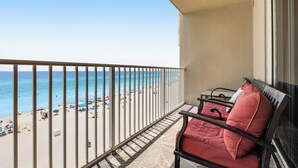 Un balcón con vista a la playa, una silla con cojín rojo y una mesita.