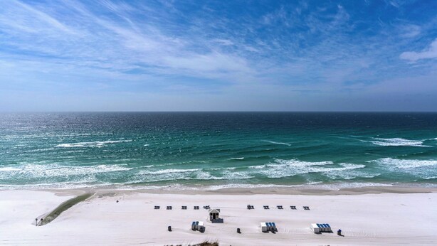 Une plage de sable blanc offrant une vue dégagée sur l’océan. Plusieurs chaises de plage et des parasols sont disposés sur le sable.