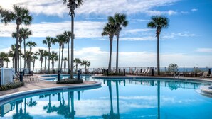 Une piscine bordée de palmiers, avec des chaises longues et un ciel dégagé.