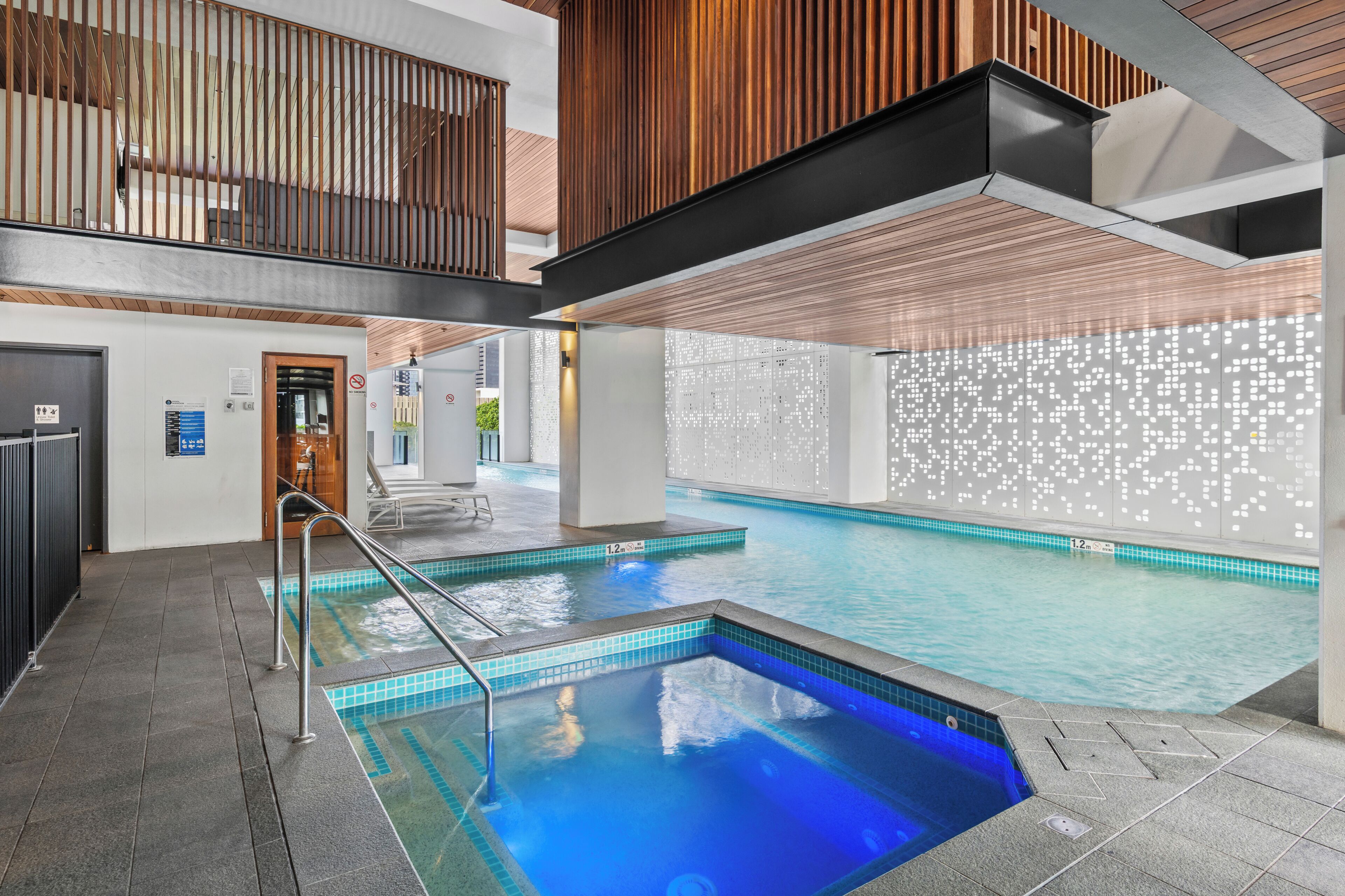 A swimming pool with a blue tint, a wooden ceiling, and a tiled wall with a light pattern.