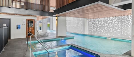 A swimming pool with a blue tint, a wooden ceiling, and a tiled wall with a light pattern.