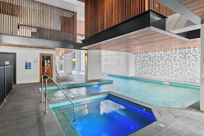 Une piscine à l’eau légèrement bleutée, un plafond en bois et un mur recouvert de carreaux formant un motif clair.