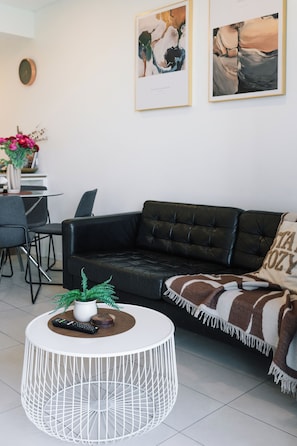 Ein stilvolles Wohnzimmer mit einem schwarzen Ledersofa, einem weißen runden Couchtisch und einem kleinen Topfpflanzen.