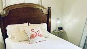 Een net opgemaakt bed met een witte sprei en twee kussens, waarvan één met een flamingo dessin.