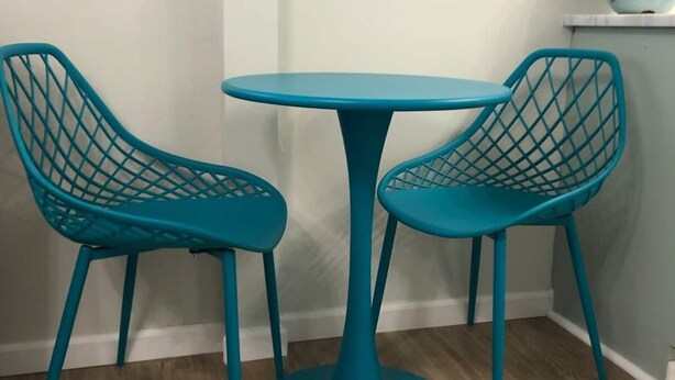 Een smaragdgroene tafel met een rond blad en een zuilvoet, omringd door twee identieke smaragdgroene stoelen met een grillig rugpatroon.