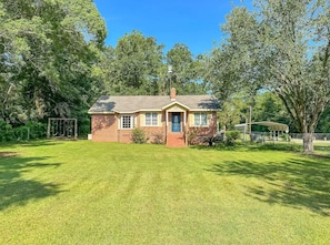 A single-story brick house with a front porch, a small lawn, and a swing set in the background. - Groups Hot Tub 4b 4b Private Fun (Tallahassee)