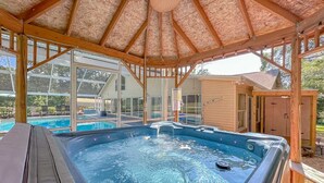 A hot tub under a wooden pergola with a glass enclosure, a pool, and a covered patio area.