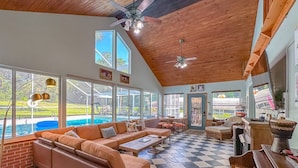A spacious living room with a checkered floor, a large sofa, a piano, and a view of a swimming pool.