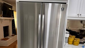 Un refrigerador de acero inoxidable en una cocina con armarios blancos y una chimenea de ladrillo.