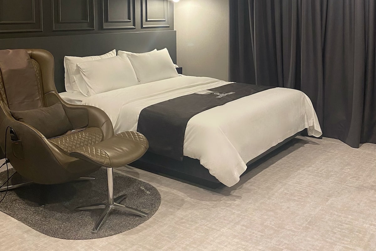 A modern hotel room with a bed, a massage chair, a round rug, and a large window with curtains.
