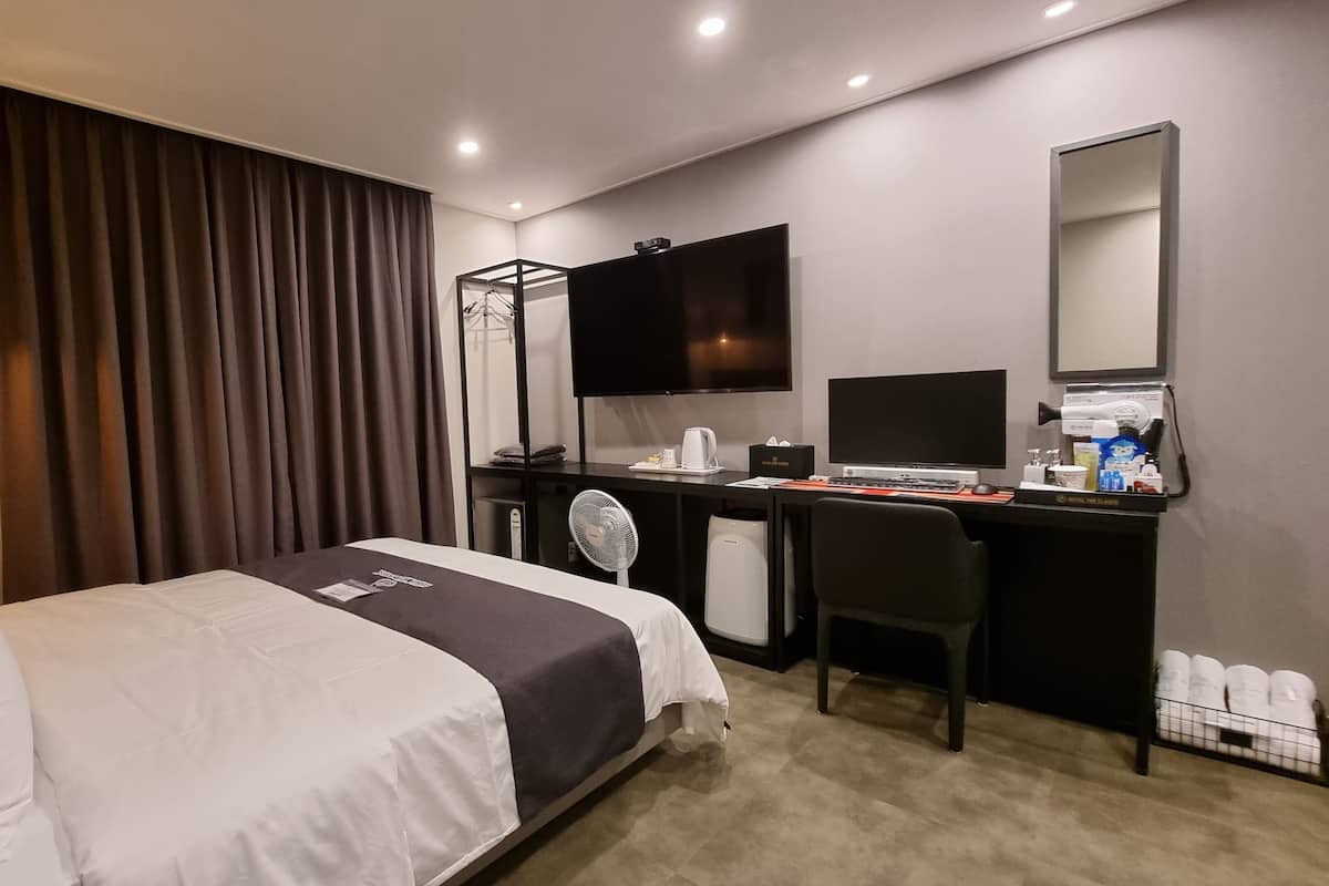 A hotel room with a bed, desk, chair, and a large mirror.