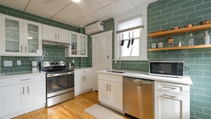 Une cuisine moderne avec des meubles blancs, des appareils en acier inoxydable et des murs recouverts de carreaux verts.