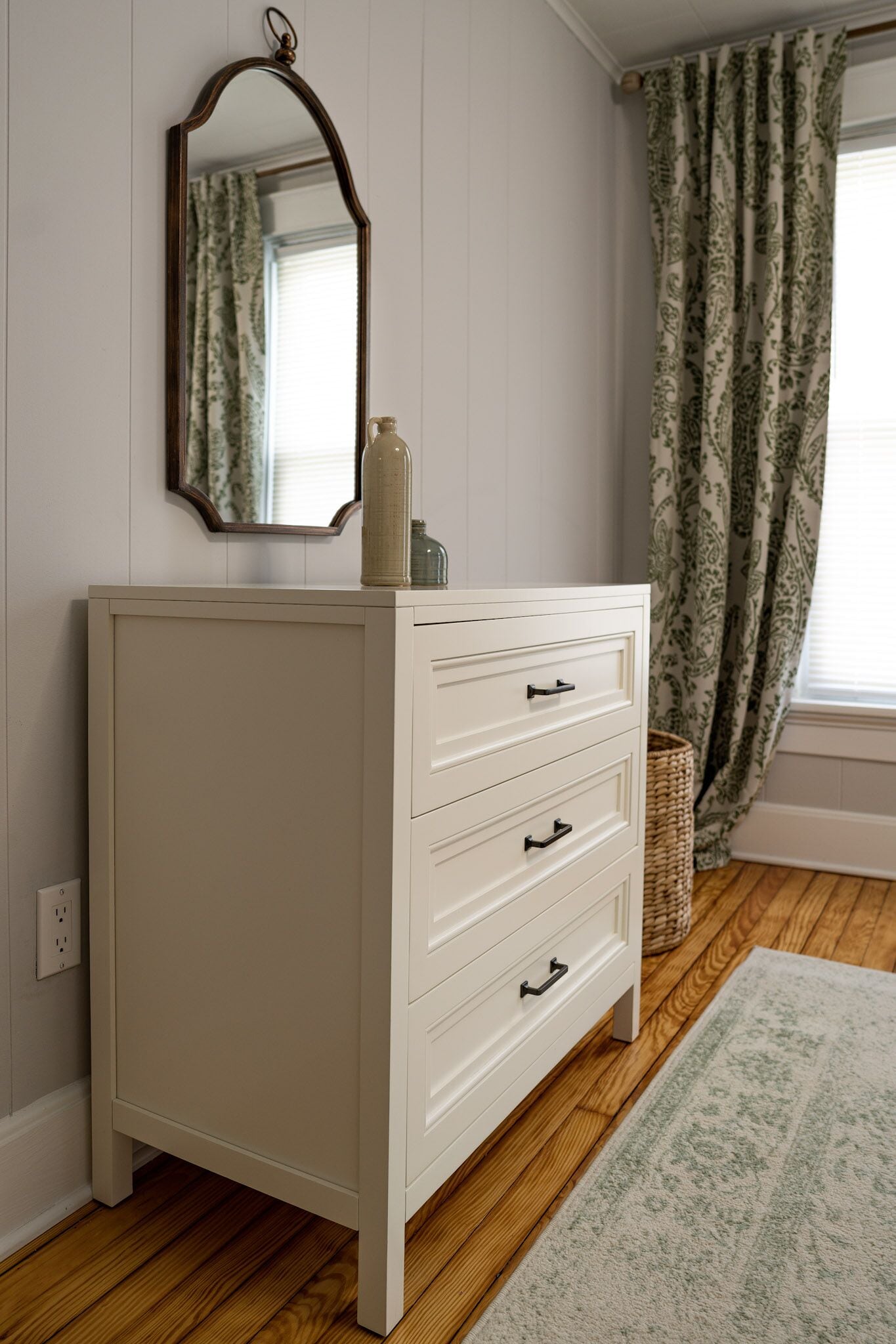 A white dresser with drawers, a mirror above it, and a woven basket on the floor.
