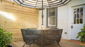 Une terrasse en bois avec une table et des chaises, placée sous un parasol à rayures, et entourée de plantes en pot.