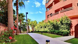 A pathway leading to a building with a red facade, surrounded by lush greenery and palm trees. - Cozy and quiet apartment (Motril)