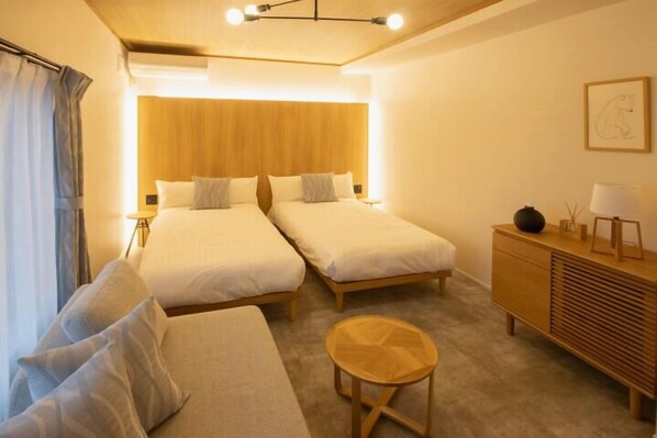 A hotel room with two beds, a wooden headboard, a small round table, a nightstand, and a dresser.