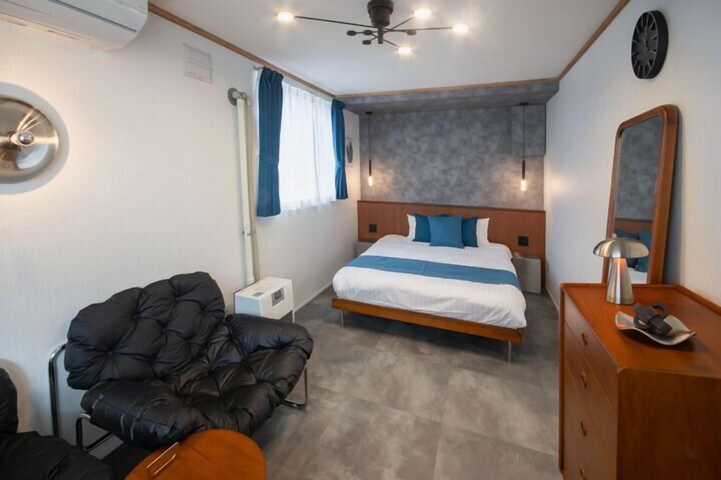 A modern bedroom with a bed, a black leather chair, a wooden dresser, and a ceiling fan.