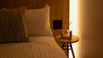 A hotel room with a bed, pillows, a bedside table with a lamp, and a wall-mounted control panel.