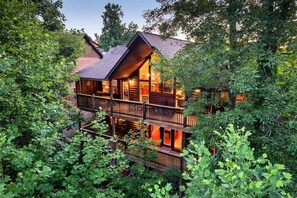 A log cabin with a balcony and a second floor, surrounded by dense foliage. - Winter Sale! Dollywood Cabin with Hot Tub & Games (Sevierville)