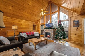 A cozy cabin interior with a fireplace, a Christmas tree, and a large window. - Winter Sale! Dollywood Cabin with Hot Tub & Games (Sevierville)