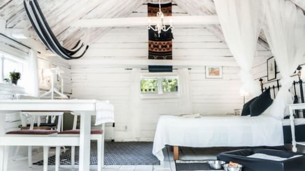 A white wooden room with a bed, a table, and a chair. There is a window and a hanging light fixture. - Toftahult Gård (farm) (Ryd)