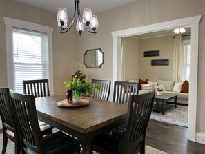 A dining area with a wooden table and chairs, a chandelier, a Christmas tree, and a living room with a sofa and a coffee table.
