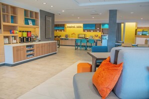 Eine moderne Hotelhalle mit Barbereich, Sitzgelegenheiten und einer Küche im Hintergrund.