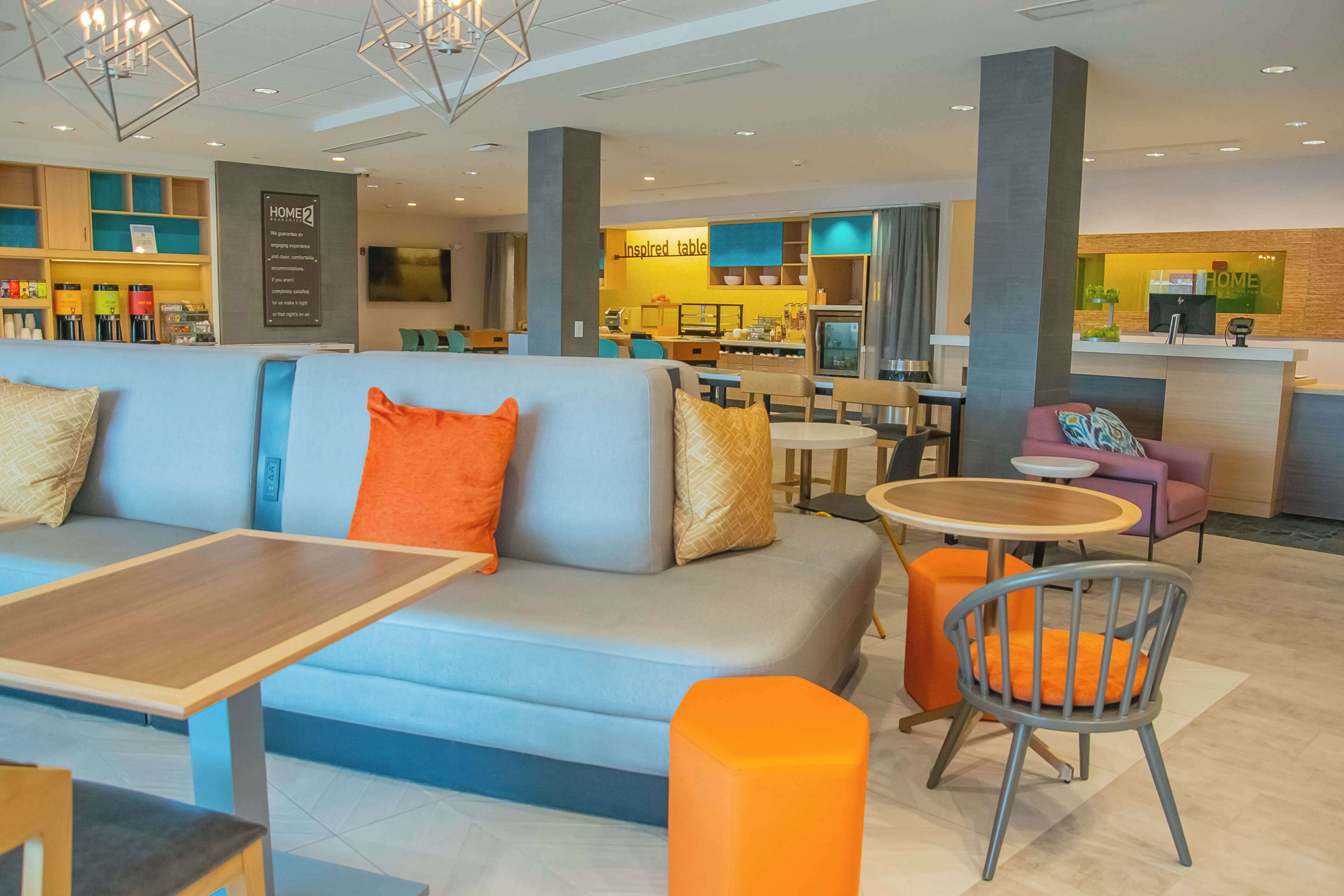 Um saguão de hotel moderno com área de estar, balcão de recepção e cozinha ao fundo.
