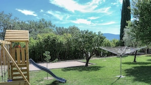 A playground with a slide and climbing structure, surrounded by grass and trees. - Gîte Les Oliviers Côté Lavande, near Vaison La Romaine  (Crestet)