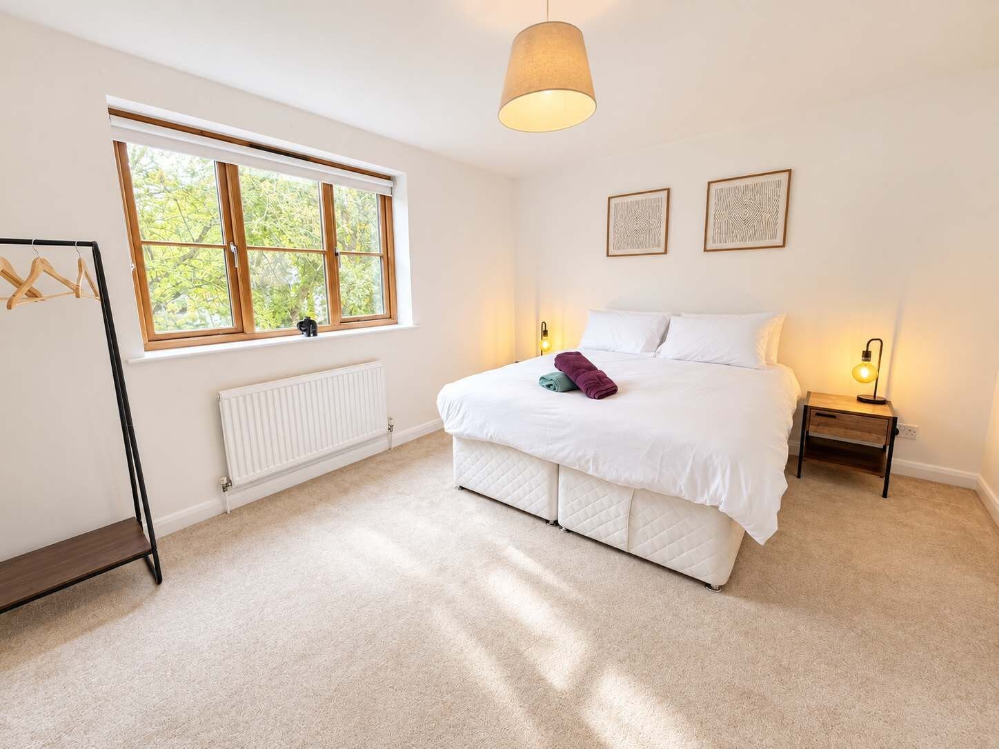 A bedroom with a bed, bedside lamps, a radiator, a window, and a hanging light fixture.