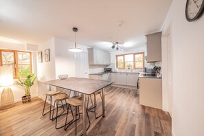 A modern kitchen with a central island, wooden stools, white cabinets, and a large window providing natural light. - Middle Ashbrook  - up to 6 bed - 3.5 bathrooms (Didcot)