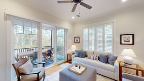 Ein geräumiges Wohnzimmer mit einer Couch, Sesseln, einem Couchtisch und einem Balkon mit Esstisch-Set.