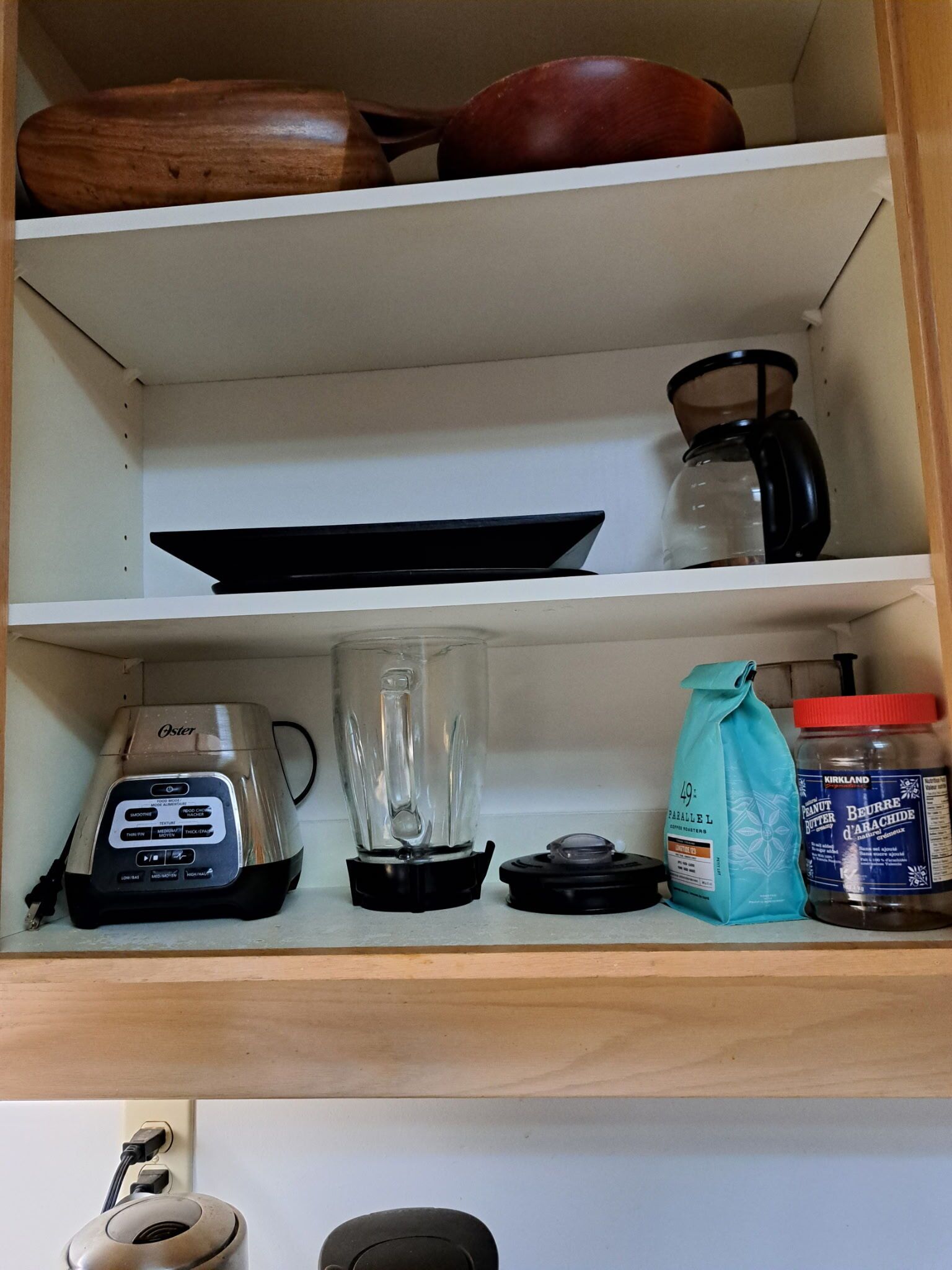 A kitchen shelf with a coffee maker, a blender, a jar of peanut butter, and a bag of flour.