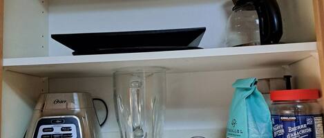 A kitchen shelf with a coffee maker, a blender, a jar of peanut butter, and a bag of flour.